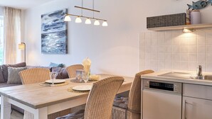 A modern kitchen with a dining area, featuring a dishwasher, a hanging light fixture, and a painting on the wall. - Hansa-residenz II Appartement 9 (Scharbeutz)