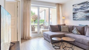 A modern living room with a grey sofa, two round wooden tables, and a large painting on the wall. - Hansa-residenz II Appartement 9 (Scharbeutz)