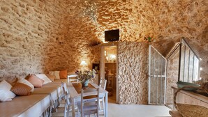Un interior acogedor con una pared de piedra, una zona de comedor con mesa y sillas, y una escalera.