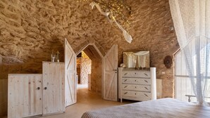 Un dormitorio rústico con paredes de piedra vista, muebles de madera y una cama con colcha a rayas.