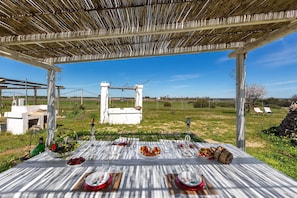 An outdoor dining area with a table set for a meal, surrounded by a pergola and a view of the countryside.