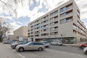 Een meerlaags woongebouw met balkons, een parkeerplaats en een winkelpand.