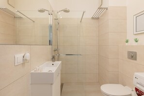 Een moderne badkamer met een douchecabine van glas, een witte wastafel en een toilet.