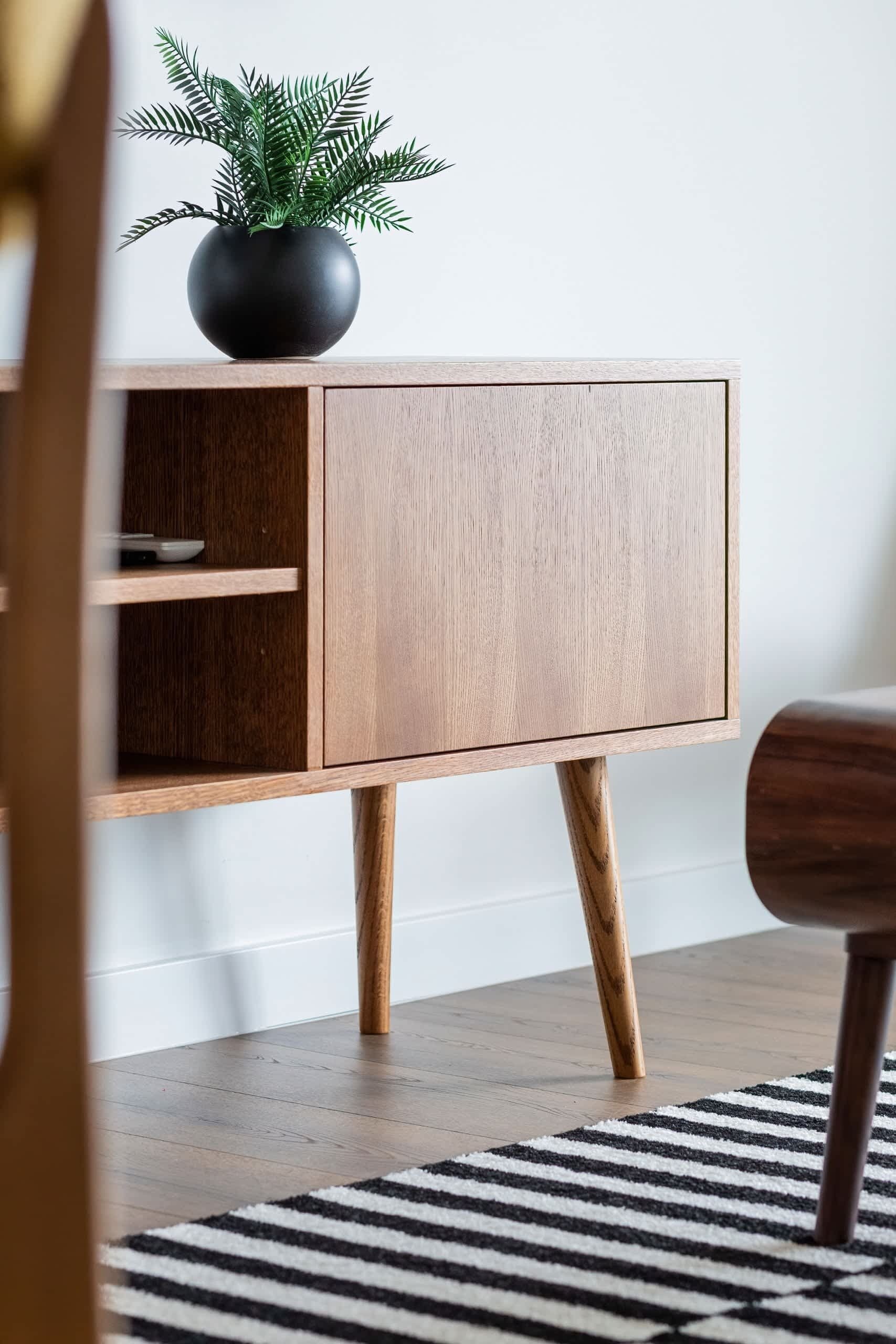 A wooden console with potted plants and minimalist decor, placed near a striped rug.