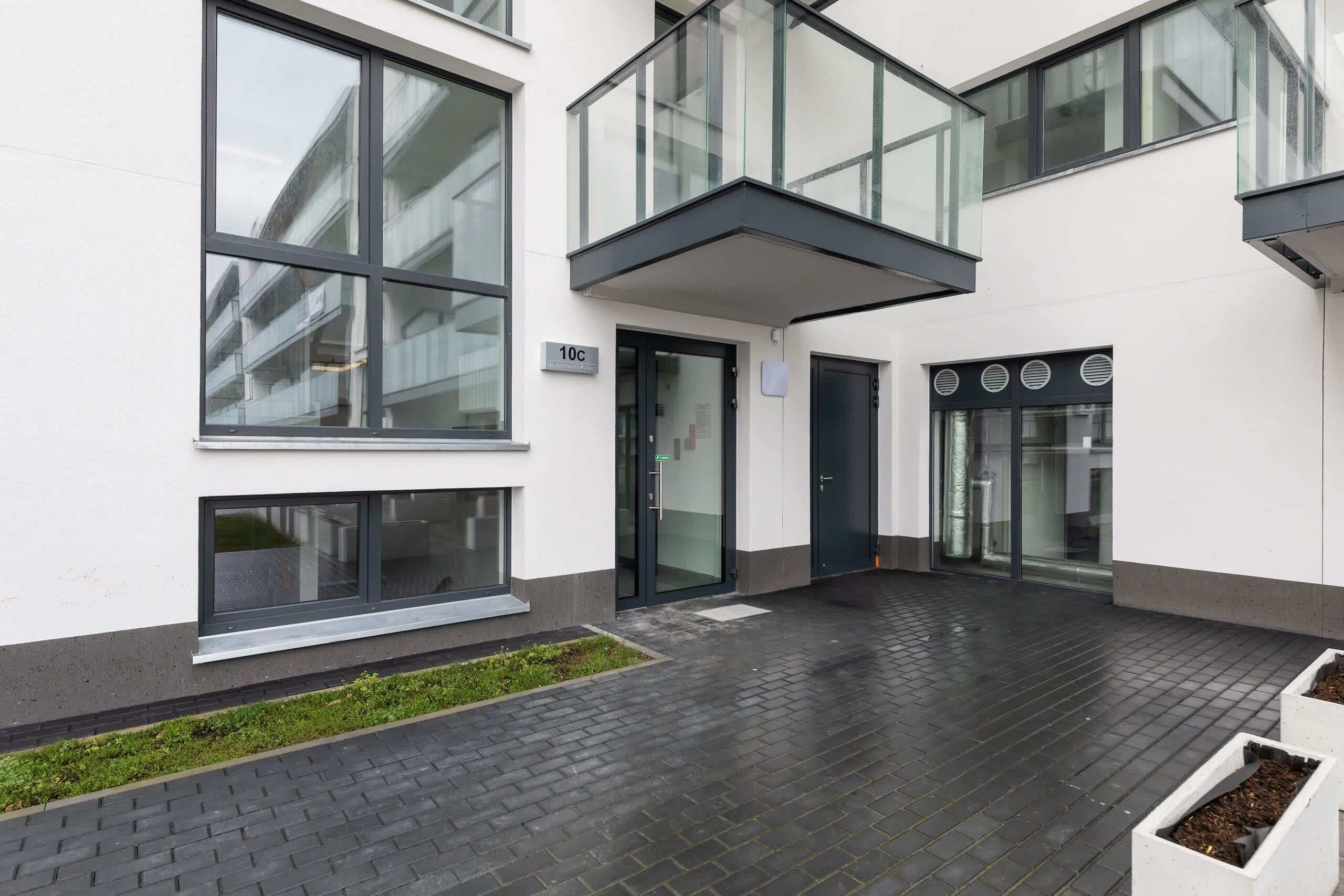 A modern building with large windows, a glass balcony, and a paved courtyard.