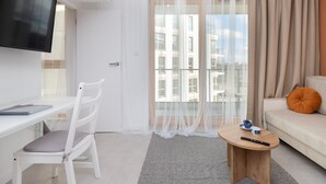 A modern living room with a white desk, a chair, a round coffee table, a sofa, and a TV mounted on the wall. - Comfortable Apartment in Gdansk | Parking | Balcony | AC (Gdańsk)