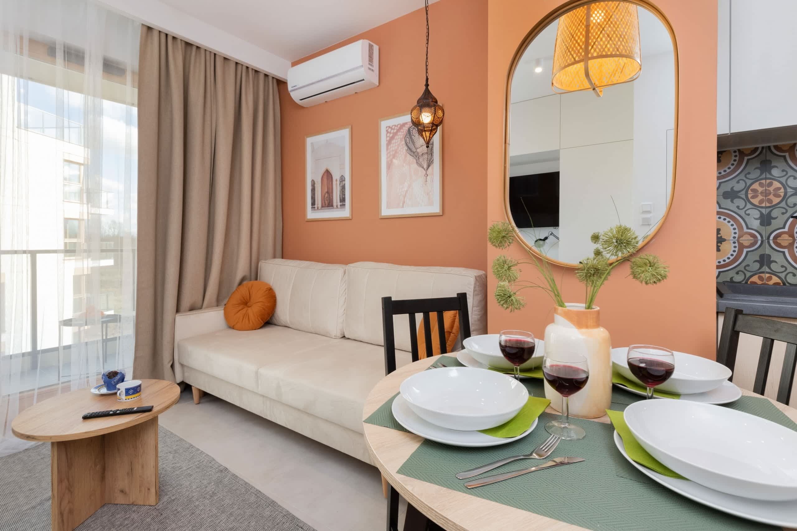 A cozy dining area with a round table, chairs, and decorative details. A large window allows natural light to brighten the warm-toned interior.