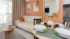 A modern living room with a sofa, a dining table set for two, and a large mirror. - Comfortable Apartment in Gdansk | Parking | Balcony | AC (Gdańsk)