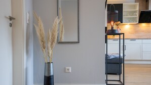 Un salon moderne avec un grand miroir, un vase contenant de l’herbe des pampas, une table noire sur laquelle est posée une lanterne, et un canapé.