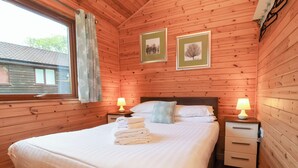 A wooden-paneled bedroom with a large bed, two bedside tables with lamps, and framed pictures on the wall. - 1 Manleigh Park (Ilfracombe)