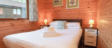Un dormitorio con paneles de madera, una cama grande, dos mesitas de noche con lámparas y cuadros en la pared.