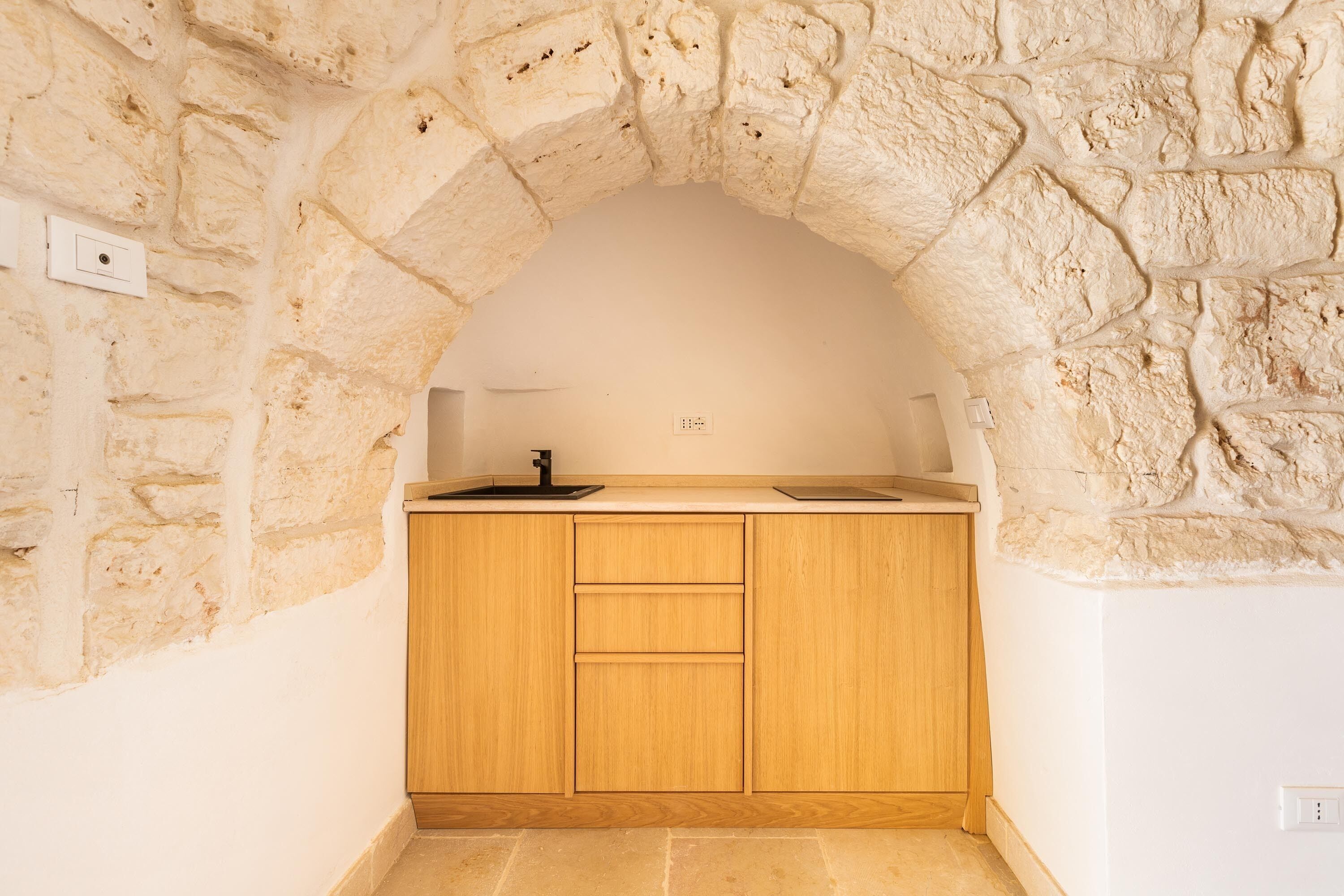 A kitchen with a stone archway, wooden cabinets, and a countertop with a sink.
