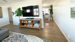 Una sala de estar moderna con una televisión de pantalla plana, un mueble de entretenimiento de madera y una zona de comedor con mesa y sillas.