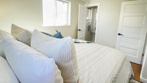 Un dormitorio con cama, almohadas, una ventana y una puerta.