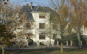 Ein zweistöckiges Gebäude mit einer symmetrischen Fassade, einem zentralen Eingang und einem sichtbaren Balkon.