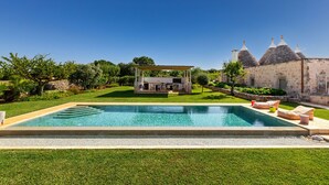 A swimming pool with a patio area, a stone building with conical roofs, and a well-maintained lawn. - 3224 Trulli Almaviva by Perle di Puglia (Cisternino)
