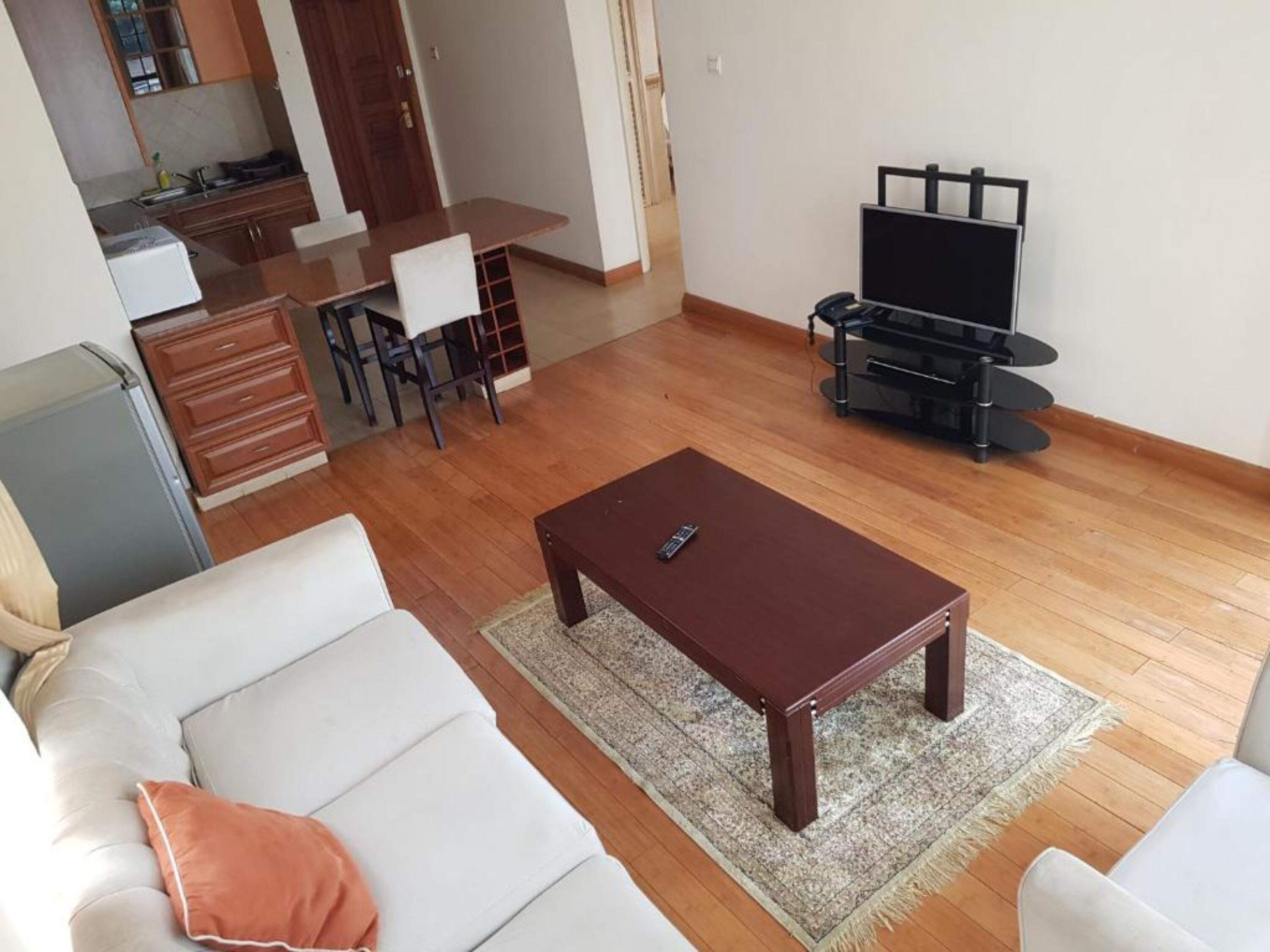 Una sala de estar con sofá, mesa de centro, mueble para televisor y una cocina al fondo.