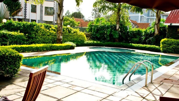 A swimming pool with a tiled deck, surrounded by well-maintained hedges and trees. - Natural Oak Apartments (Nairobi)