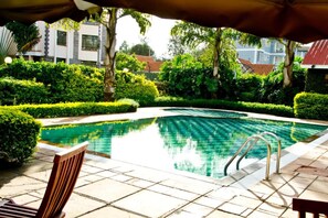 Una piscina con borde de baldosas, rodeada de setos y árboles bien cuidados.