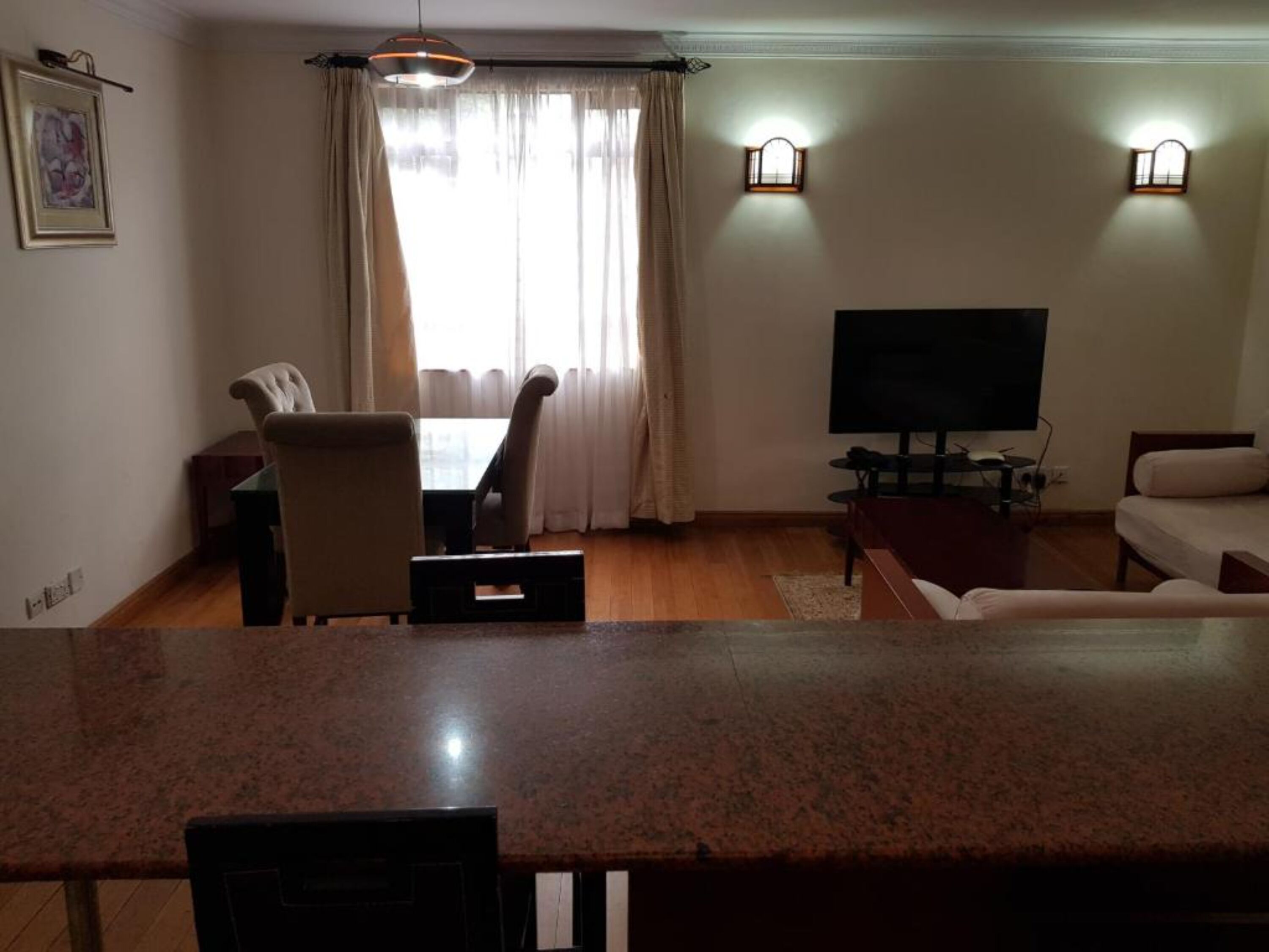 Una sala de estar con televisor, sofá, sillón y ventana con cortinas.