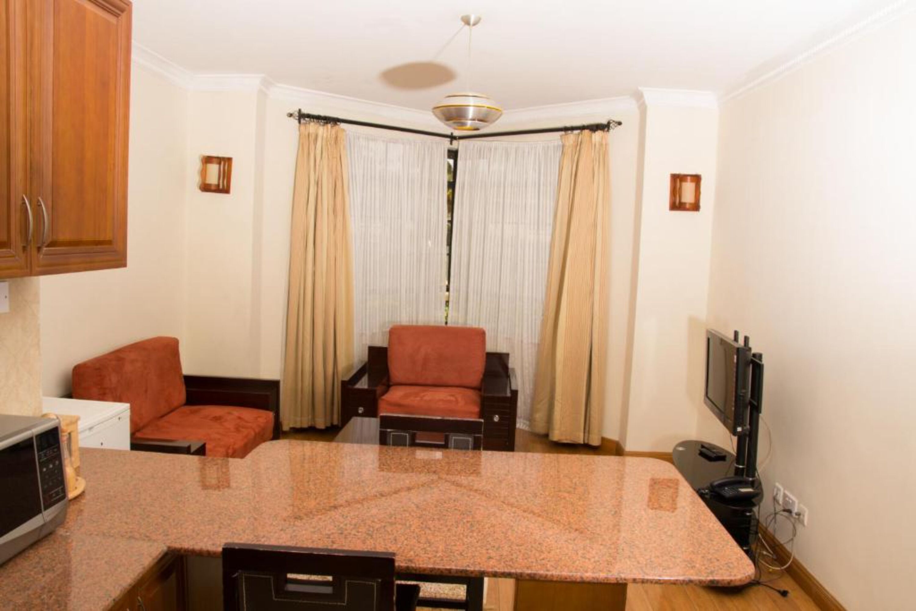 A compact kitchen with a granite countertop, wooden cabinets, a microwave, and a television.