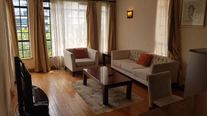 A living room with a sofa, two armchairs, a coffee table, and a TV. - Natural Oak Apartments (Nairobi)