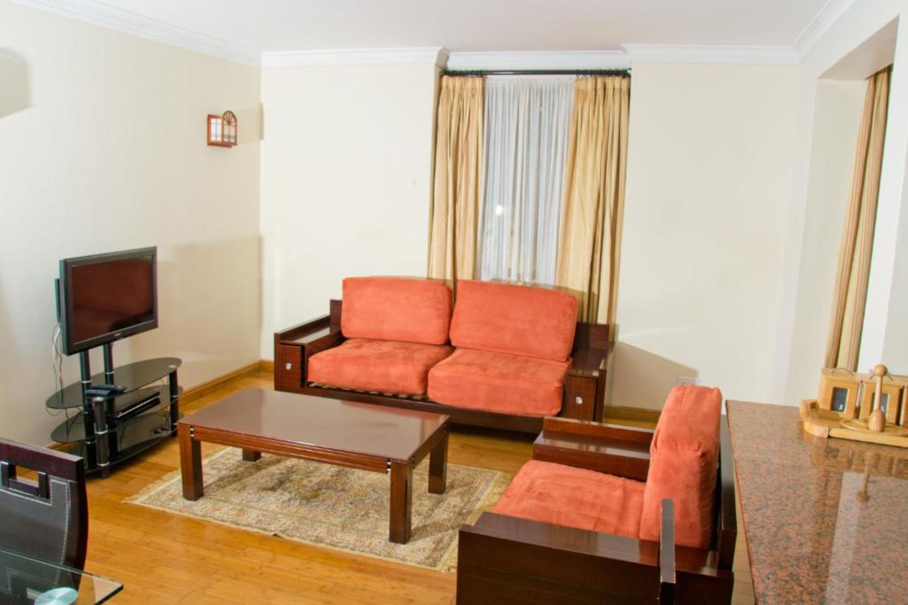 Uma sala de estar com sofá, mesa de centro, televisão e uma pequena mesa com objetos decorativos.