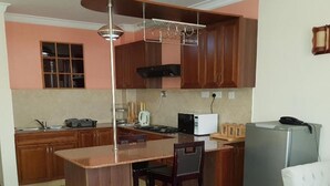 A compact kitchen with wooden cabinets, a built-in island, and a dining area with a table and chairs. - Natural Oak Apartments (Nairobi)