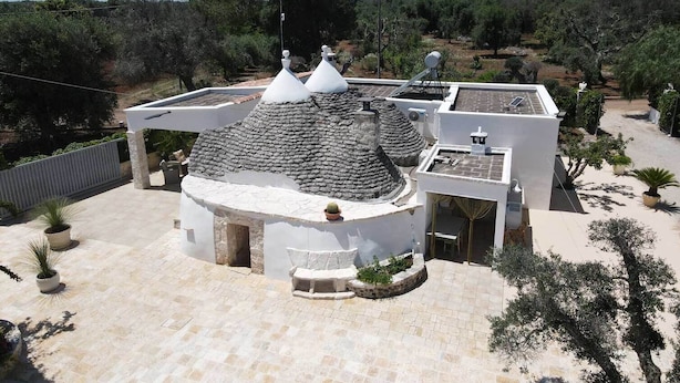 Une maison moderne avec un toit en pierre, des murs blancs et un jardin agrémenté de plantes en pot.