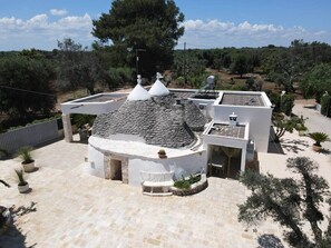 A modern house with a stone roof, white walls, and a garden with potted plants. - 3229 Trullo Mimosa by Perle di Puglia (San Michele Salentino)