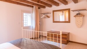 Una camera da letto con soffitto in legno, un letto con coperta grigia, un comò in legno, uno specchio e un appendiabiti.
