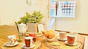 Colazione servita con un cesto in vimini, una moka, una ciotola di croissant e una finestra con persiane a griglia.