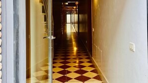 Un passadís amb un paviment a quadres, bigues de sostre de fusta i portes de vidre que donen a una habitació.