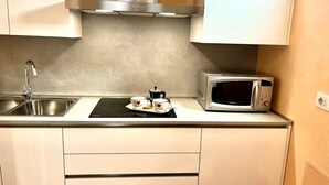 Cuina amb un vàser d'acer inoxidable, un microones i un petit espai per al cafè, amb tasses i una olla.