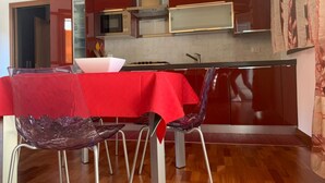Cocina moderna con armarios de madera, microondas y estufa. Hay una mesa de comedor con mantel rojo y un bol de vidrio morado.