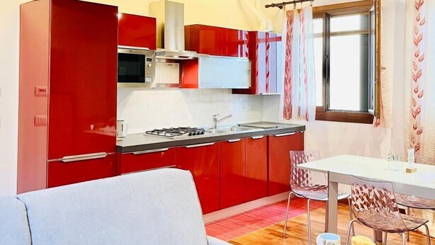 Cocina pequeña con armarios rojos, estufa a gas y una ventana con cortinas.
