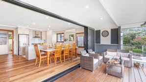 A spacious kitchen with wooden flooring, a dining area with wooden chairs, and a patio with wicker furniture. - Tanapaser – spacious centrally located home with fireplace (Currarong)