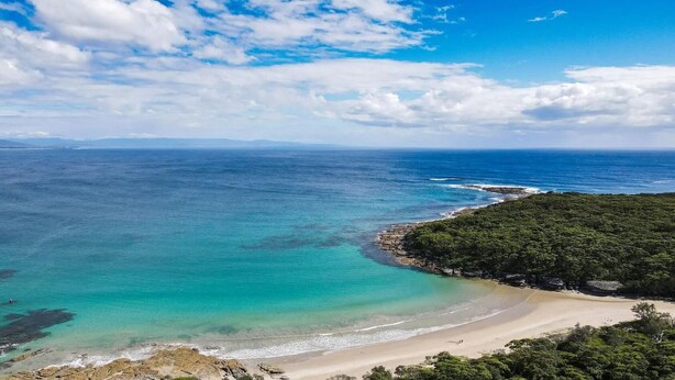 A coastal landscape with a beach, clear turquoise waters, and a forested area. - Tanapaser – spacious centrally located home with fireplace (Currarong)