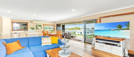 A spacious living room with a blue sofa, wooden coffee table, and a television displaying a beach scene.