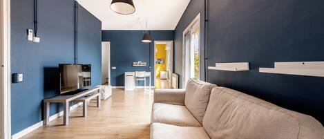 A modern living room with a beige sofa, a flat-screen TV, and a dining area with a table and chairs.