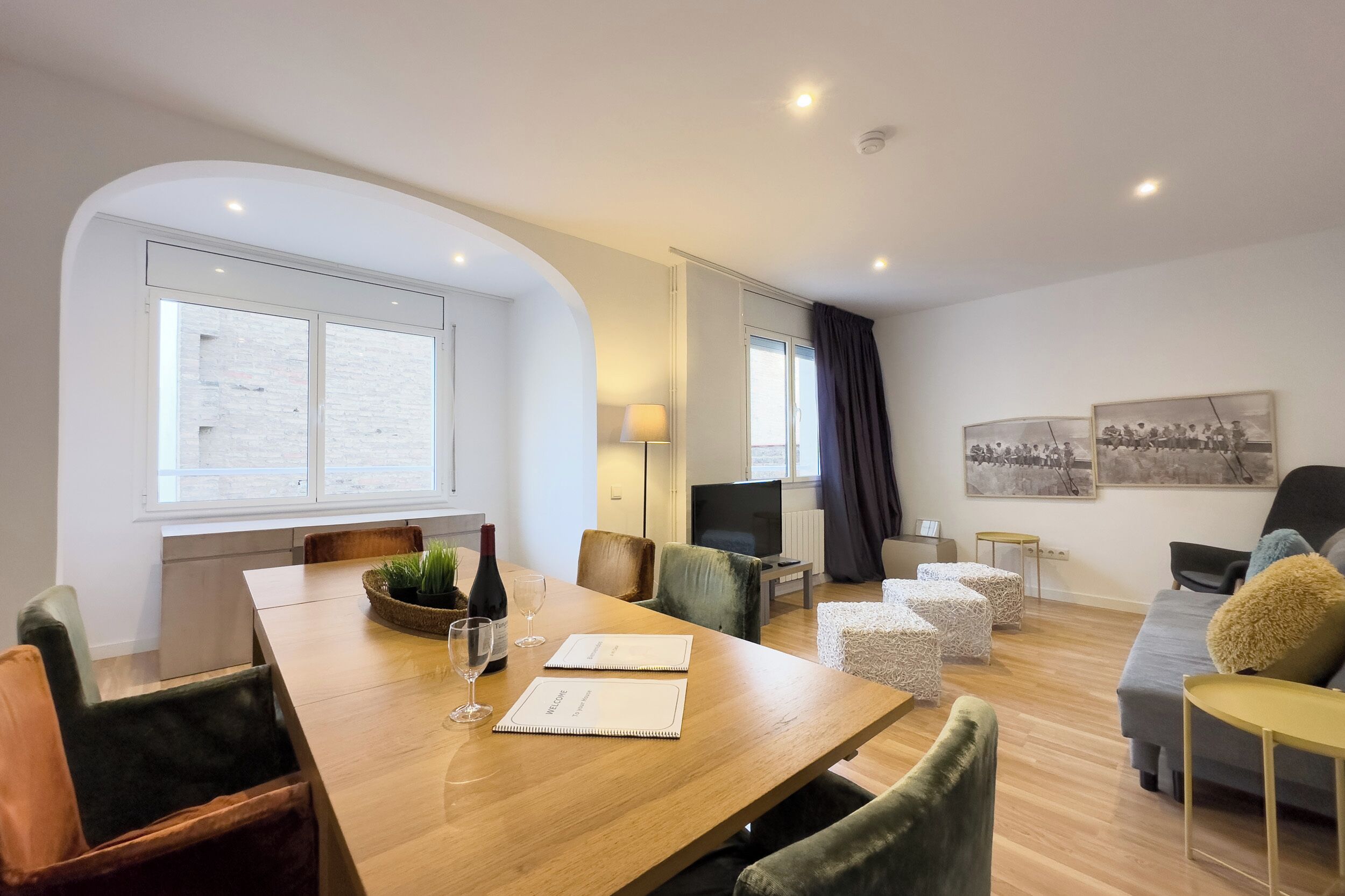 A modern hotel room with a wooden dining table, comfortable seating, a flat-screen TV, and artwork on the walls.