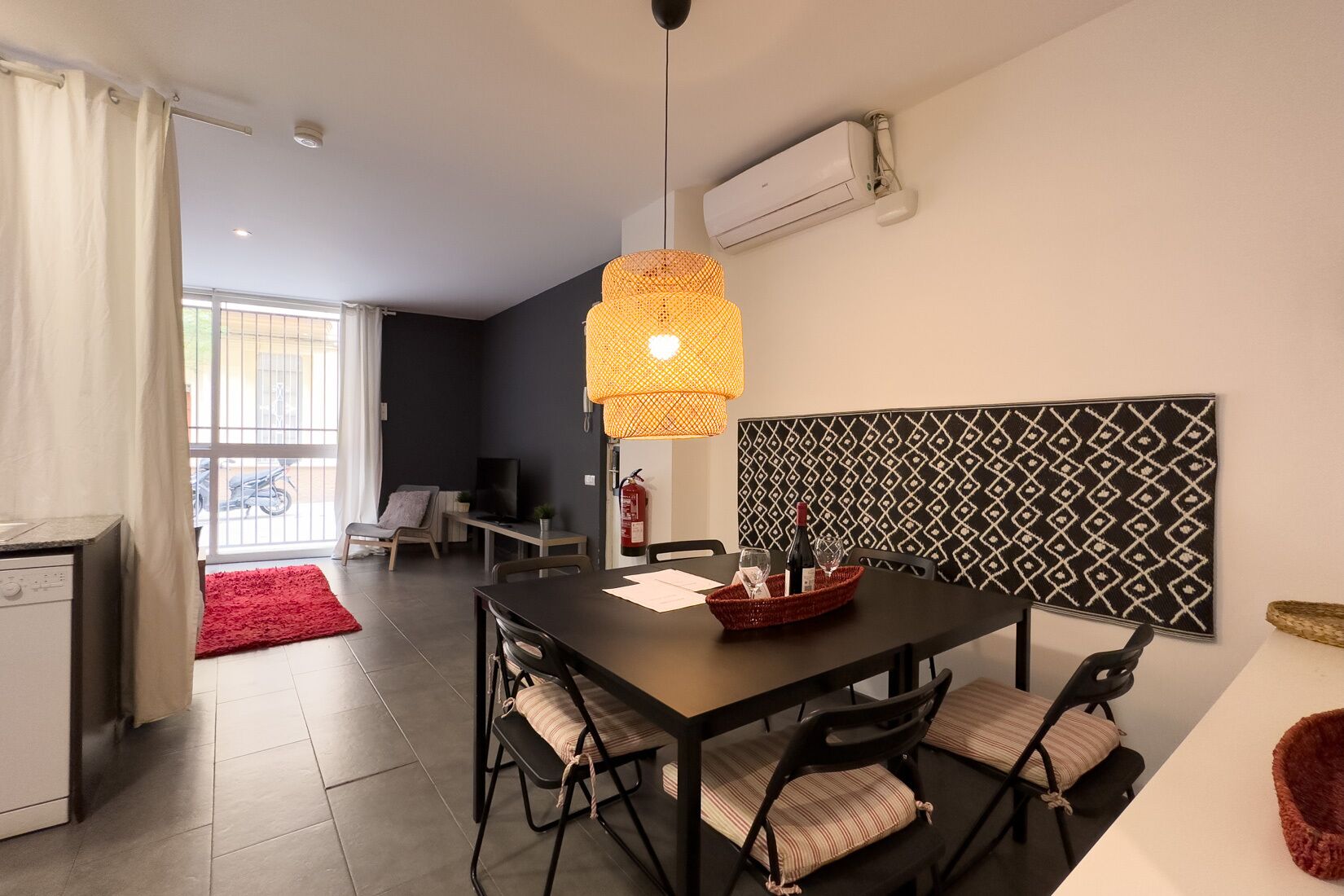 Un comedor moderno con una mesa negra, cuatro sillas, un tapete rojo y una lámpara colgante.