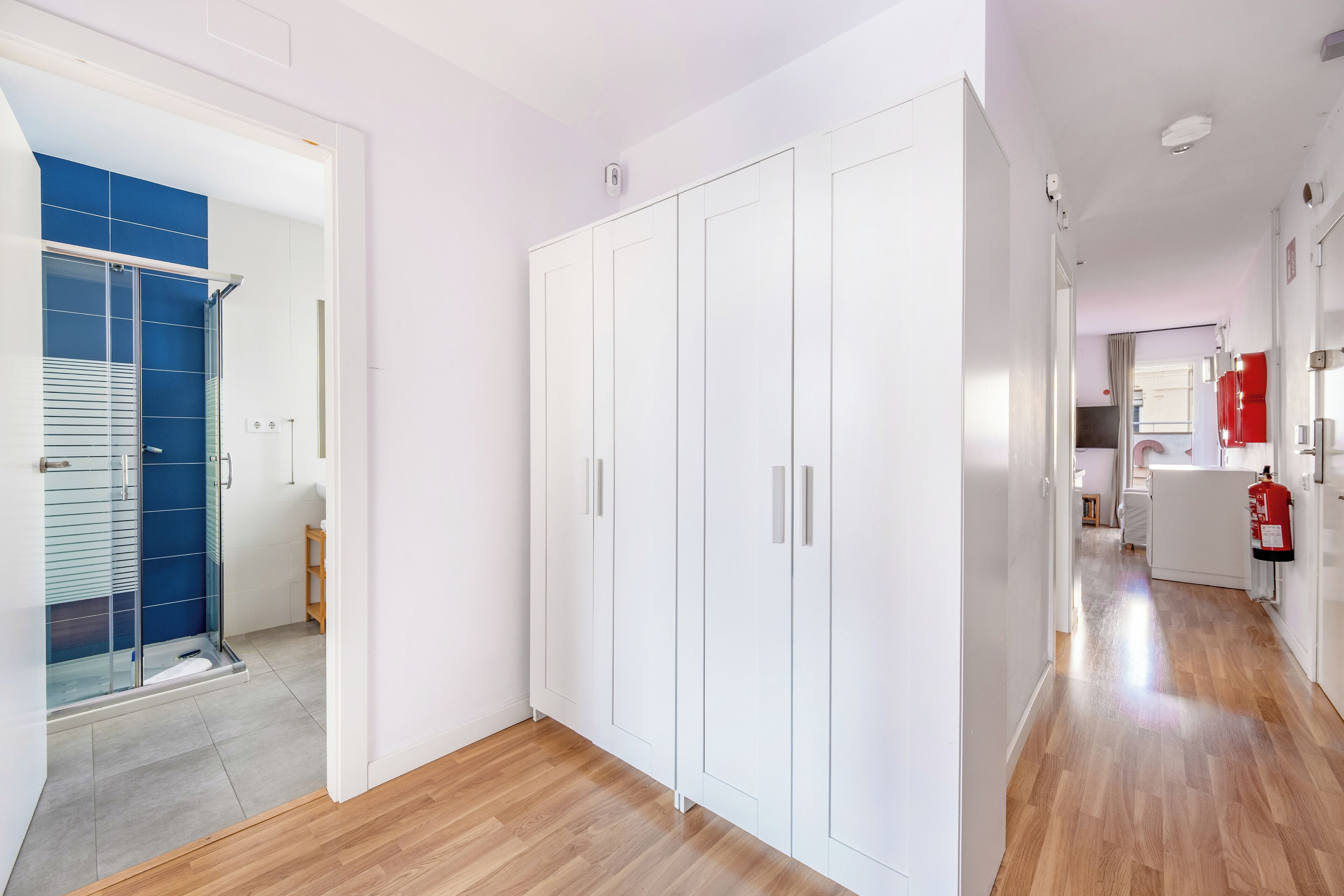 Un pasillo con suelo de madera, paredes blancas y una zona de ducha con azulejos azules.