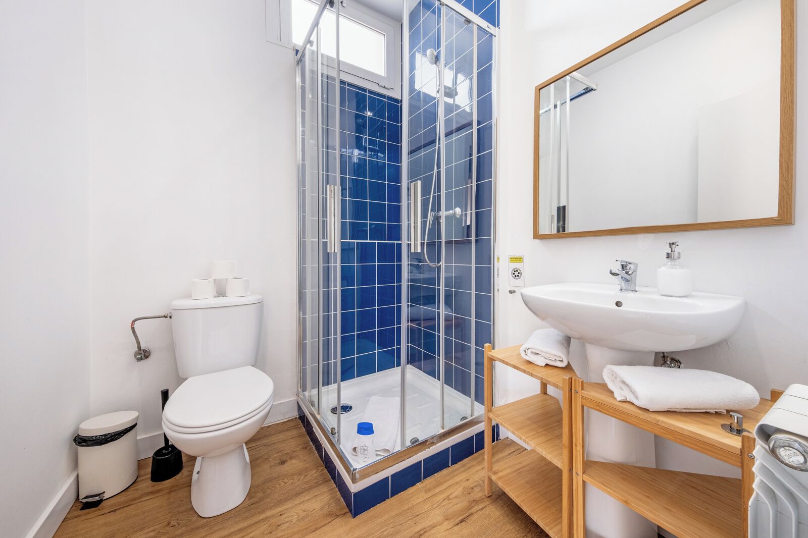 Een moderne badkamer met een glazen douchecabine, een witte wastafel en een houten wastafelmeubel.