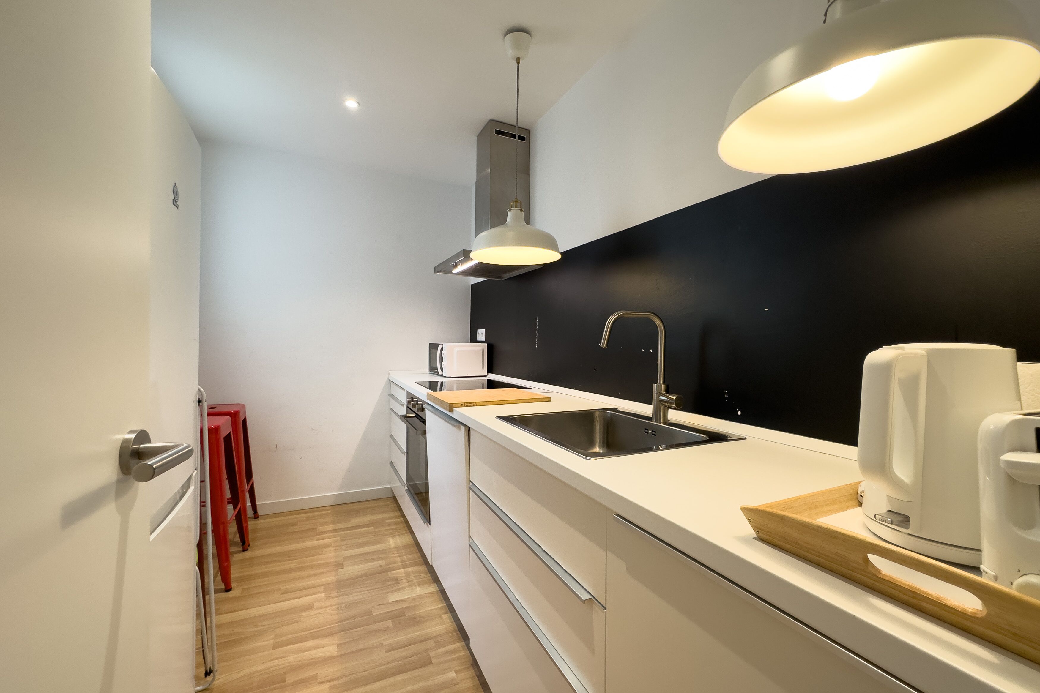 Una cocina moderna con armarios blancos, salpicadero negro, electrodomésticos de acero inoxidable y encimera de madera.