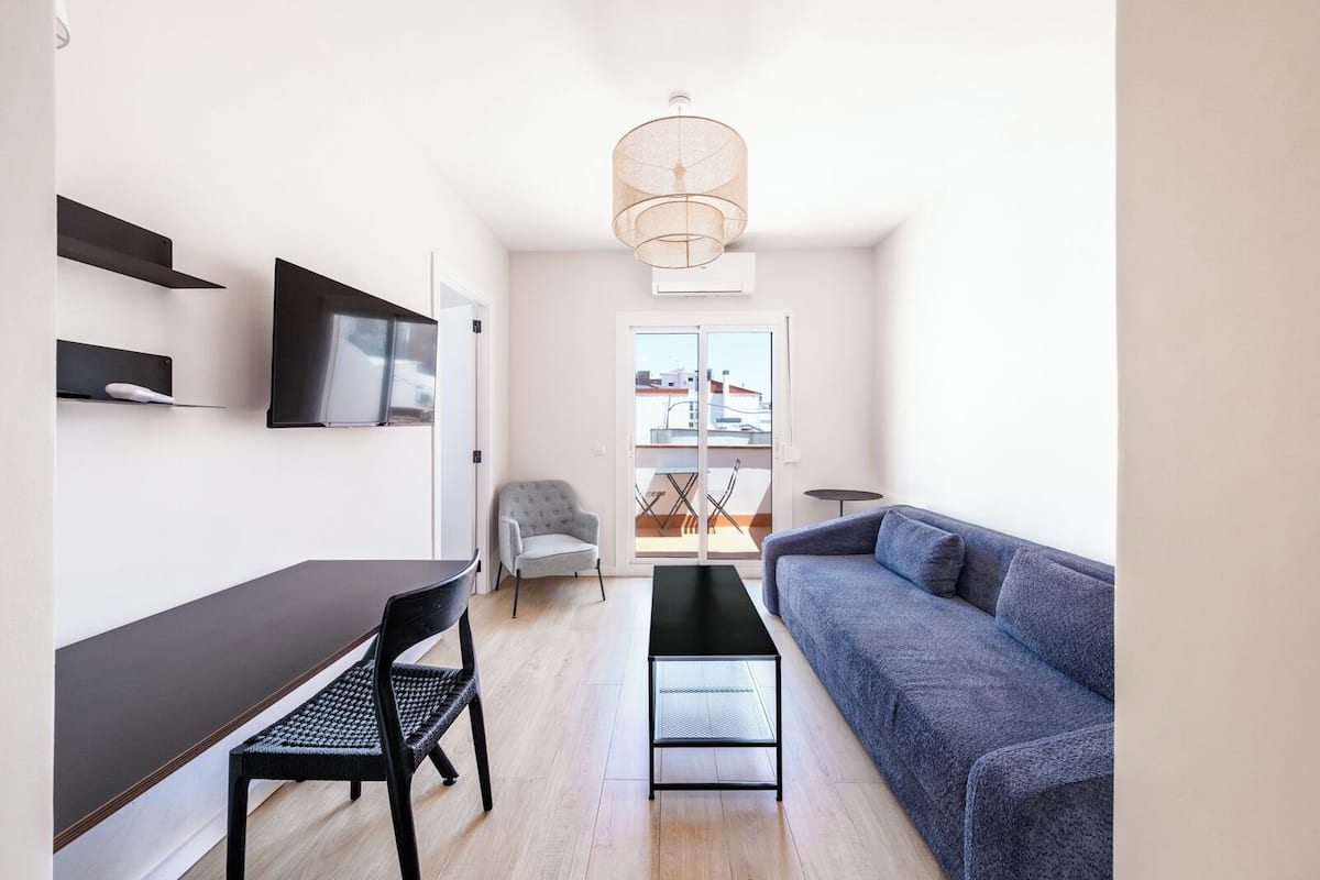 A modern, compact living space with a sofa, a dining table, and a TV mounted on the wall.
