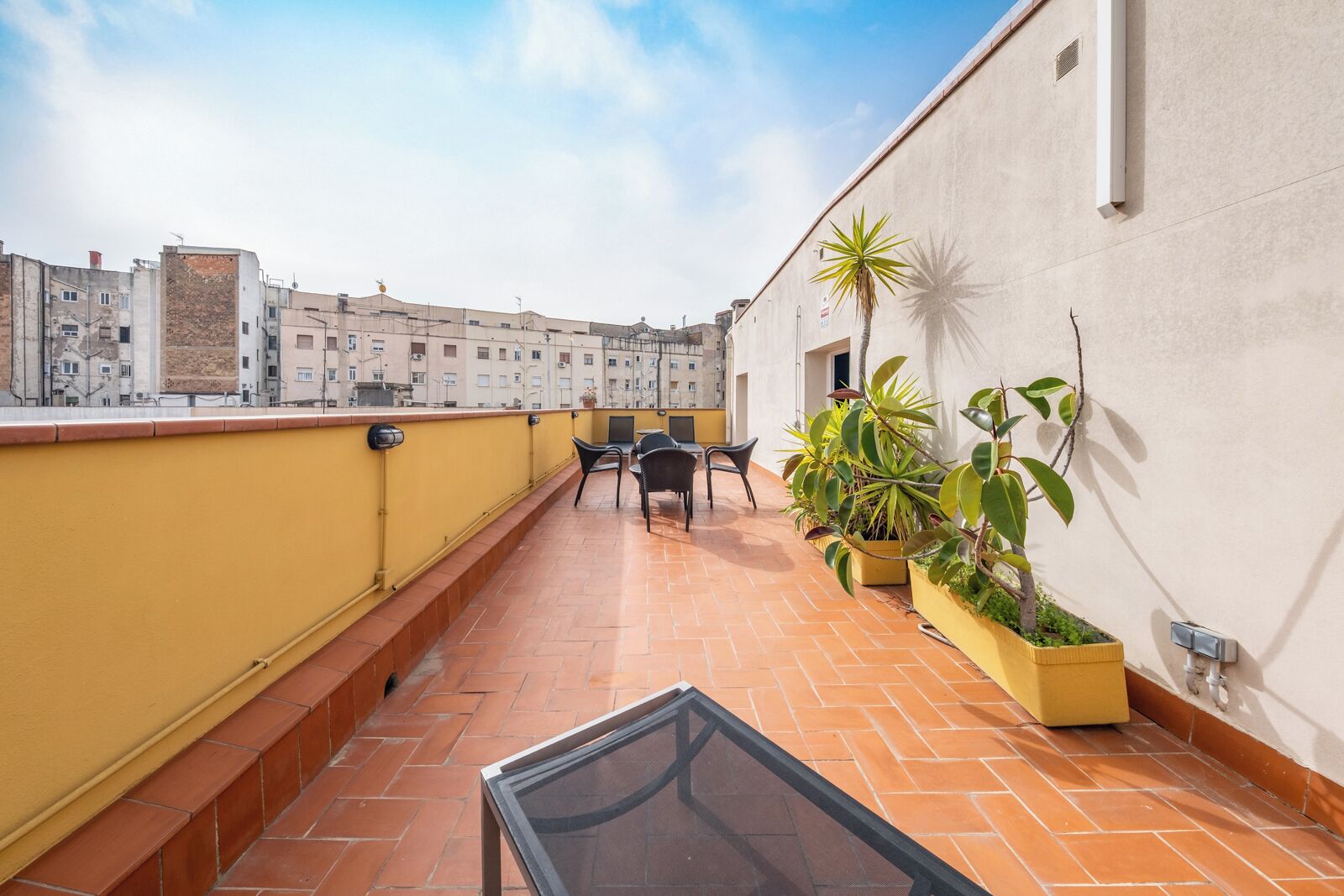 Une terrasse sur le toit avec une rambarde jaune, une table avec des chaises et des plantes en pot.