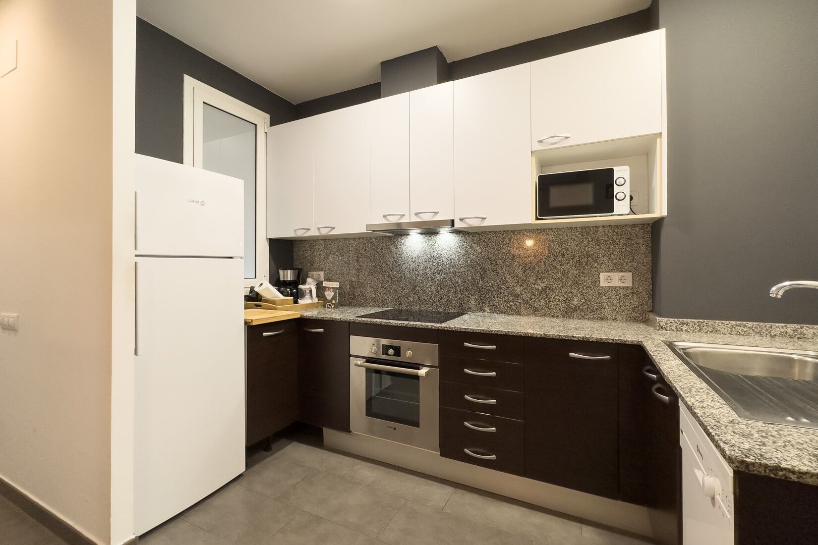 Eine moderne Küche mit weißen Schränken, einer Granit-Arbeitsplatte, einer eingebauten Mikrowelle, einer Edelstahl-Spüle und einem Backofen.