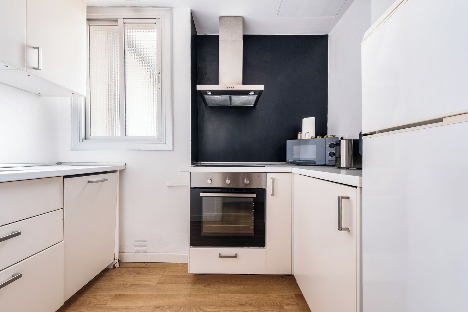 A compact kitchen with white cabinetry, a built-in oven, a microwave, and a black backsplash.