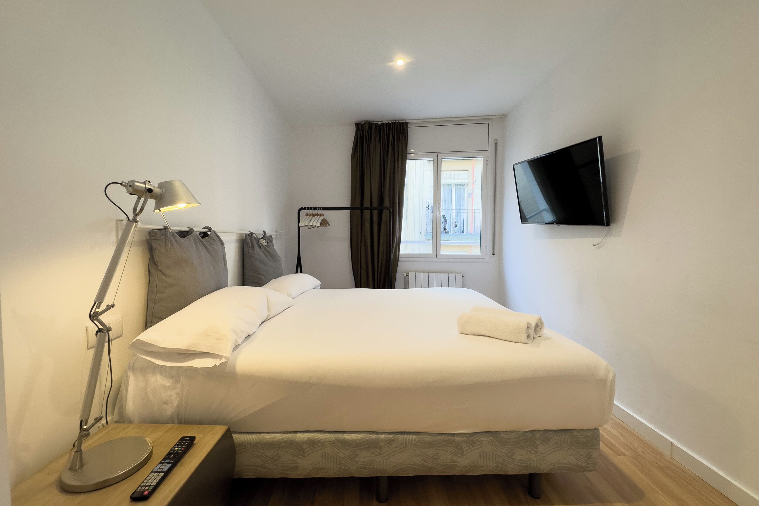 Une chambre d’hôtel avec un lit, un bureau avec une lampe, une télévision et une fenêtre avec des rideaux.